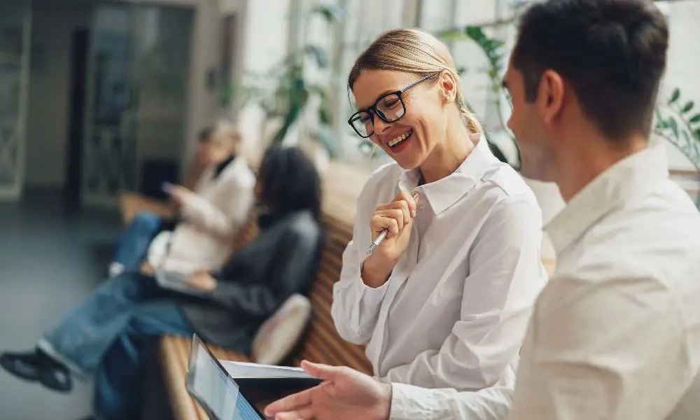 A man and a women looking at a laptop on a desk in a modern office environment.